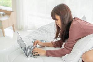 asiatische Frau, die zu Hause mit Laptop auf dem Bett arbeitet