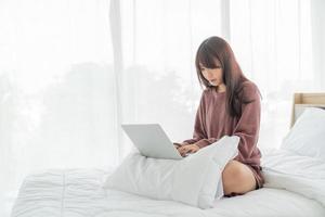 asiatische Frau, die zu Hause mit Laptop auf dem Bett arbeitet