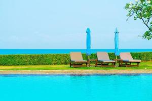 Stuhlpools oder Liegen und Sonnenschirme rund um den Pool mit Meereshintergrund - Ferien- und Urlaubskonzept