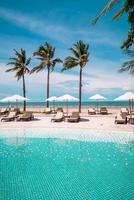 Stuhlpools oder Liegen und Sonnenschirme rund um den Pool mit Meereshintergrund - Ferien- und Urlaubskonzept