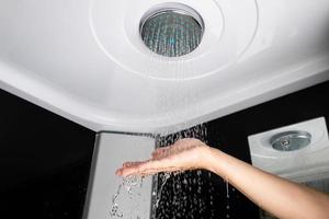 Ein Mädchen hält ihre Hand über den Wasserdruck eines Duschkopfes, Regendusche Badezimmer