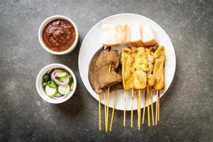 Schweinefleisch-Satay mit Erdnusssauce und Gurken, Gurkenscheiben und Zwiebeln in Essig foto