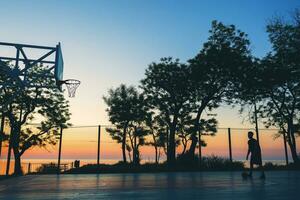 cool schwarz Mann tun Sport, spielen Basketball auf Sonnenaufgang, Silhouette foto