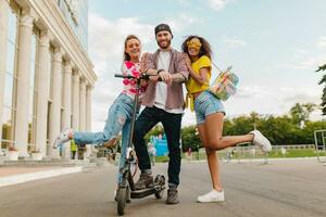 glücklich jung Unternehmen von lächelnd freunde Gehen im Straße mit elektrisch trete Roller foto