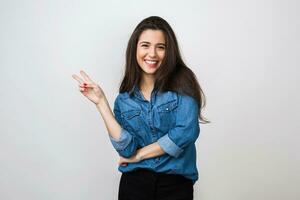 Porträt von jung ziemlich Frau lächelnd im Blau Denim Hemd auf Weiß Hintergrund, Glücklich, positiv Stimmung, isoliert, aufrichtig lächeln, lange Haar, zeigen Frieden Zeichen, positiv Stimmung foto