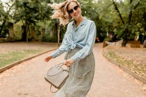 attraktiv blond lächelnd Frau Gehen im Park im stilvoll Outfit foto