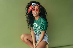 attraktiv schwarz afrikanisch amerikanisch Frau posieren im stilvoll Hipster Outfit auf Grün Hintergrund foto