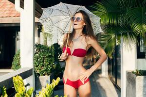 jung Frau mit schön schlank Körper tragen rot Bikini Badeanzug halten Spitze Sonne Regenschirm foto