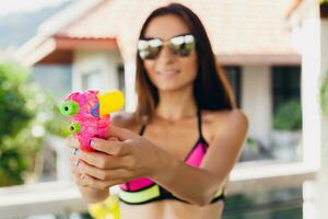 ziemlich schlank Frau spielen mit Wasserpistole Spielzeug beim Schwimmbad auf Sommer- tropisch Ferien foto