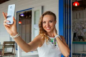 attraktiv Frau im Weiß Kleid im Sommer- Cafe im Sonnenbrille mit Telefon nehmen Foto