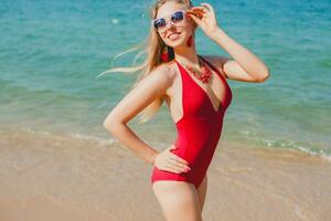 jung schön blond Frau Sonnenbaden auf Strand im rot Schwimmen Anzug, Sonnenbrille foto