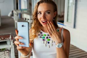 attraktiv Frau im Weiß Kleid im Sommer- Cafe im Sonnenbrille mit Telefon nehmen Foto