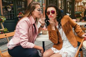 zwei jung stilvoll Frauen Sitzung beim Cafe, reden, Klatschen, stilvoll modisch Outfit foto