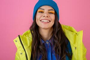 Porträt von attraktiv lächelnd stilvoll Frau posieren im Winter Mode aussehen auf Rosa Hintergrund im hell Neon- Gelb Jacke, tragen Blau gestrickt Hut, gekleidet im warm Kleider foto