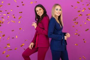 zwei attraktiv Frauen feiern Neu Jahr auf violett Hintergrund im stilvoll bunt Abend Anzüge von lila und Blau Farbe, freunde haben Spaß zusammen, Mode Trend, golden Konfetti Party Stimmung foto