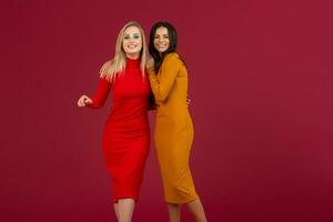 schön stilvoll Frauen freunde im Gelb und rot Herbst Winter Mode gestrickt Kleid posieren isoliert auf rot Studio Hintergrund foto