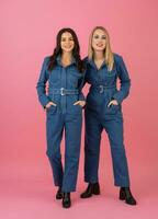 zwei aufgeregt attraktiv Mädchen freunde aktiv Frauen posieren auf Rosa Hintergrund im Denim insgesamt haben Spaß zusammen Mode Trend foto