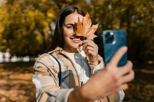 attraktiv jung Frau Gehen im Herbst tragen Jacke mit Telefon foto