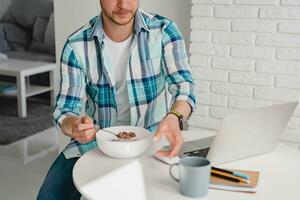 Mann im Hemd Sitzung im Küche beim Zuhause beim Tabelle Arbeiten online auf Laptop foto