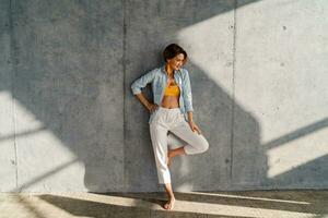 lächelnd glücklich schön Frau posieren gegen Beton Mauer auf sonnig Tag Sommer- Mode Stil Trend foto
