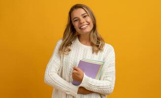 jung lächelnd ziemlich blond Frau posieren mit Bücher auf Gelb Studio Hintergrund isoliert, glücklich Ausbildung, tragen Weiß Sweatshirt foto