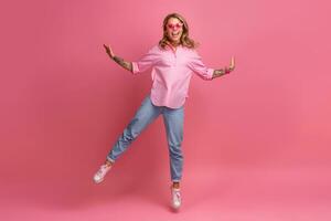 blond ziemlich Frau im Rosa Hemd und Jeans lächelnd Springen foto