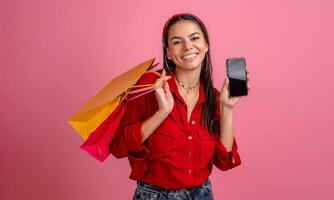 spanisch schön Frau im rot Hemd lächelnd halten halten Einkaufen Taschen und Smartphone foto