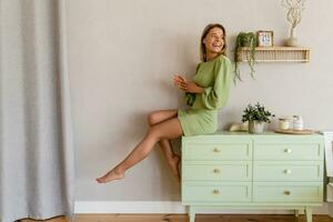 jung stilvoll lächelnd Frau im Grün Sommer- Kleid im modern Innere Wohnung Zuhause foto