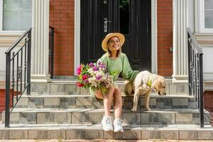 schön jung Frau im Sommer- Stil Outfit lächelnd glücklich Gehen mit Blumen im Stadt Straße foto