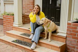 glücklich lächelnd Frau im Gelb Sweatshirt Gehen beim ihr Haus mit ein Hund golden Retriever foto