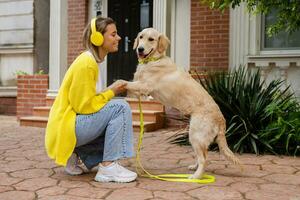 Frau im Gelb Sweatshirt Gehen beim ihr Haus mit ein Hund Hören zu Musik- im Kopfhörer foto