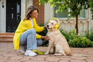 Frau im Gelb Sweatshirt Gehen beim ihr Haus mit ein Hund Hören zu Musik- im Kopfhörer foto