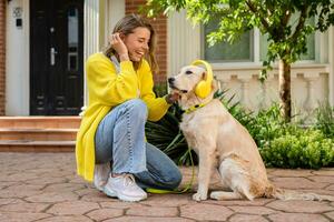 Frau im Gelb Sweatshirt Gehen beim ihr Haus mit ein Hund Hören zu Musik- im Kopfhörer foto