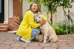 Frau im Gelb Sweatshirt Gehen beim ihr Haus mit ein Hund Hören zu Musik- im Kopfhörer foto