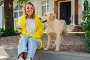 glücklich lächelnd Frau im Gelb Sweatshirt Gehen beim ihr Haus mit ein Hund golden Retriever foto