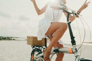 jung attraktiv lächelnd Frau im Weiß Kleid Reiten auf tropisch Strand auf Fahrrad foto