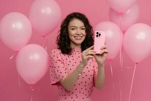 ziemlich jung Frau posieren isoliert auf Rosa Studio Hintergrund mit Rosa Luft Ballons und Smartphone foto