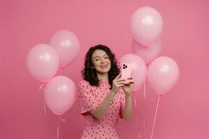 ziemlich jung Frau posieren isoliert auf Rosa Studio Hintergrund mit Rosa Luft Ballons und Smartphone foto