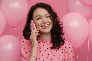 ziemlich jung Frau posieren isoliert auf Rosa Studio Hintergrund mit Rosa Luft Ballons und Smartphone foto