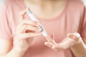 asiatische Frau mit Lanzette am Finger zur Überprüfung des Blutzuckerspiegels durch Glukosemeter, Gesundheitswesen und Medizin, Diabetes, Glykämie-Konzept foto