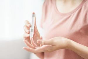 asiatische Frau mit Lanzette am Finger zur Überprüfung des Blutzuckerspiegels durch Glukosemeter, Gesundheitswesen und Medizin, Diabetes, Glykämie-Konzept foto