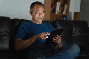 Mann sitzt auf dem Sofa, verwendet Tablet-Computer für die Arbeit oder entspannt sich zu Hause. Arbeit von zu Hause aus Konzept. foto