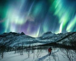 Mann Reisender Bergsteigen auf schneebedeckten Hügel mit Aurora Borealis am Nachthimmel auf der Insel Senja foto