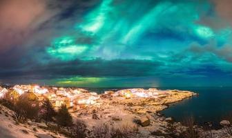 Norwegisches Dorf, das an der arktischen Küste mit Nordlichtern leuchtet foto