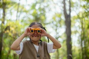glücklich wenig asiatisch Mädchen suchen voraus und lächelnd Kind mit das Fernglas im das Park. Reise und Abenteuer Konzept. Freiheit, Ferien foto