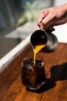 Barista gießt Milch in ein Glas Eiskaffee foto