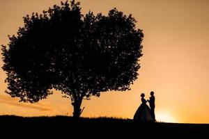Silhouetten eines glücklichen jungen Paares und eines Mädchens auf einem Hintergrund von orangefarbenem Sonnenuntergang foto