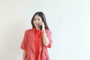 Porträt von schön asiatisch Frau tragen rot Outfit während Berufung mit lächelnd Ausdruck foto