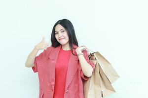 Porträt von schön asiatisch Frau tragen rot Outfit gestikulieren Tragen viele von Einkaufen Taschen mit glücklich Ausdruck foto