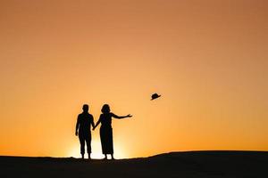 Silhouetten eines glücklichen jungen Paares auf einem Hintergrund des orangefarbenen Sonnenuntergangs in der Sandwüste foto